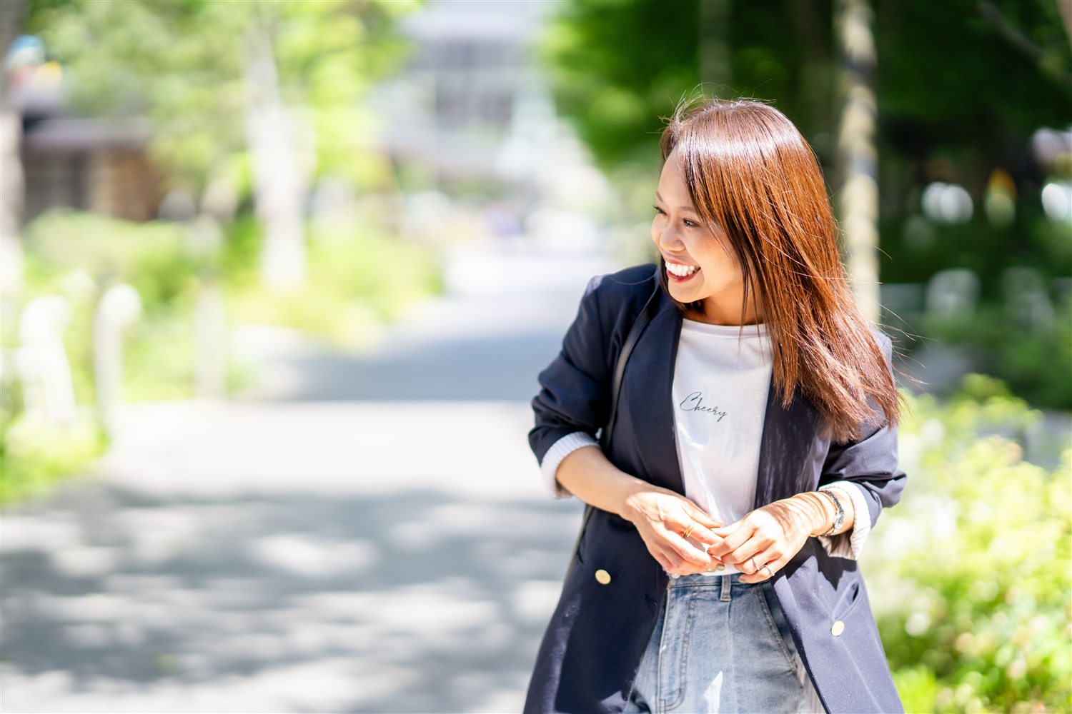 緑の中で横を向いて自然に笑うまいさん。左側に木漏れ日の余白が広がる写真